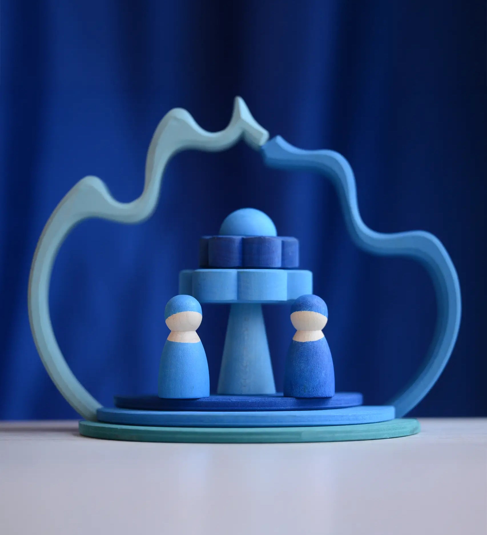 2 Grimms wave shaped pieces leaning on each other making a display with 2 blue peg dolls and other loose pieces 