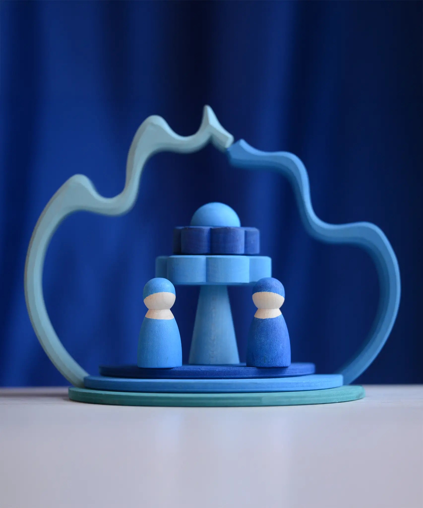 2 Grimms wave shaped pieces leaning on each other making a display with 2 blue peg dolls and other loose pieces 