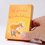 Adult hand holding the Grimms letter supplementary card set box showing the fox illustration showing scale