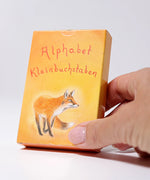 Adult hand holding the Grimms letter supplementary card set box showing the fox illustration showing scale