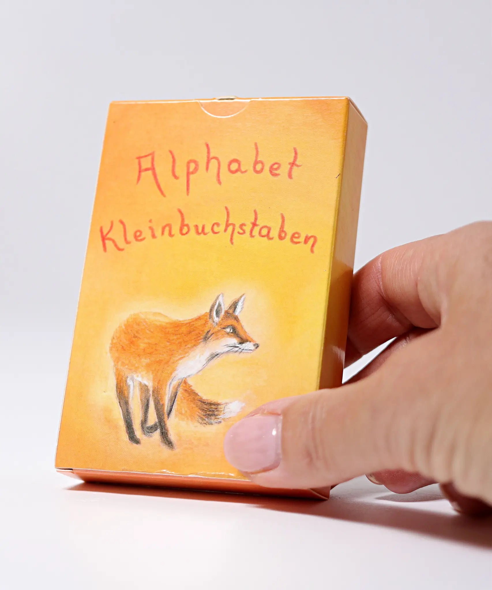 Adult hand holding the Grimms letter supplementary card set box showing the fox illustration showing scale