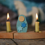 A close up of a Grimms Matryoshka star doll decorative figure inserted into the wooden celebration ring with Grimms candles either side available at Babipur.