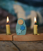 A close up of a Grimms Matryoshka star doll decorative figure inserted into the wooden celebration ring with Grimms candles either side available at Babipur.