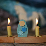 A Grimm's Matryoshka Stars Decorative Figure placed in between two lit candles on a natural celebration ring. 