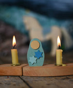 A Grimm's Matryoshka Stars Decorative Figure placed in between two lit candles on a natural celebration ring. 