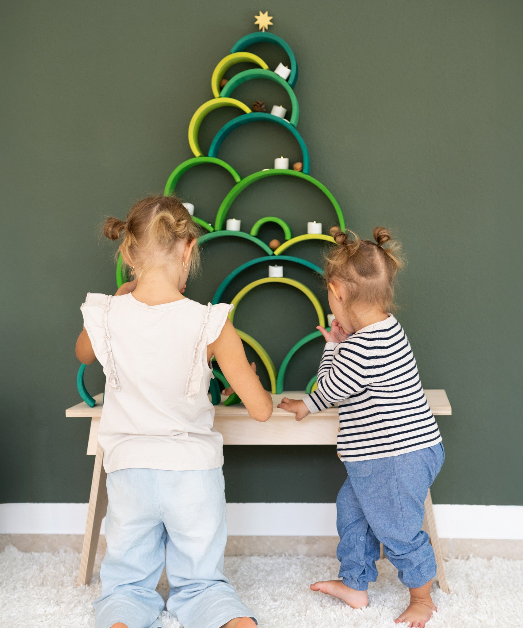 2 children making a Christmas tree stack using pieces from the meadow and forest Grimms rainbow pieces. Both of these sets are available at Babipur.