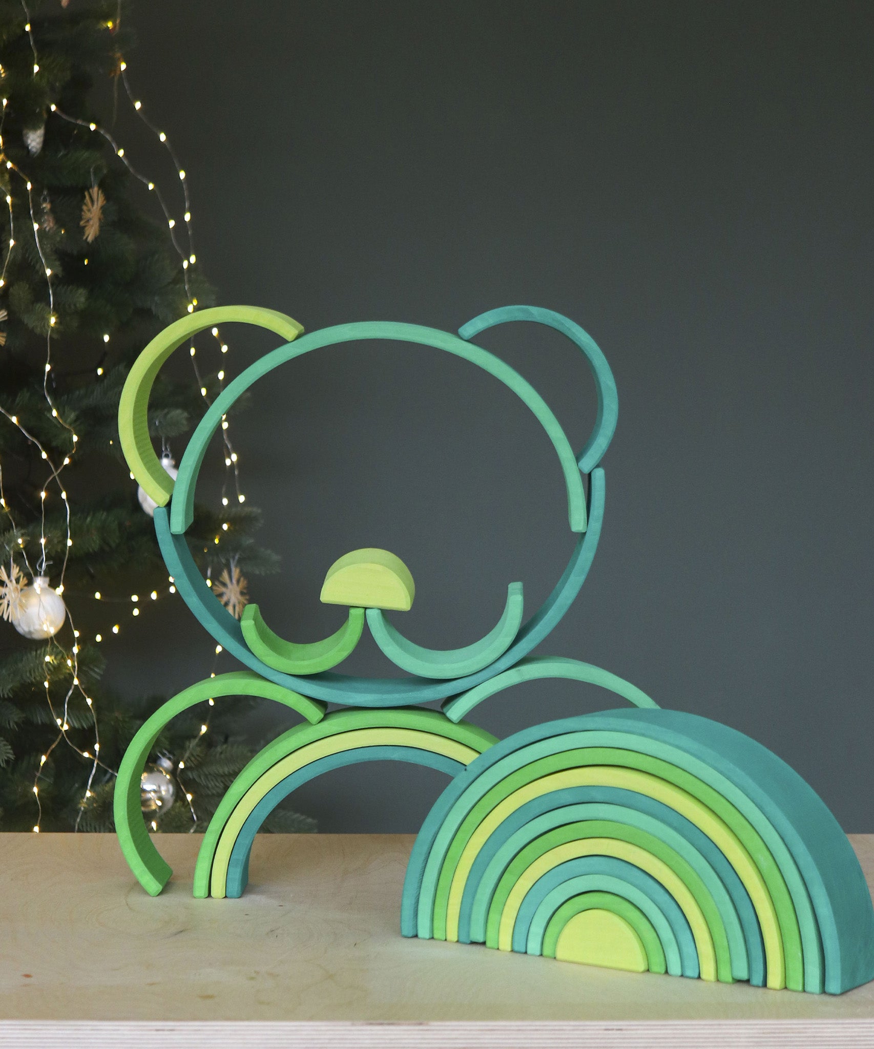 A stack shaped like a teddy bear's face made from the pieces of the Grimms meadow large green wooden rainbow set available at Babipur.