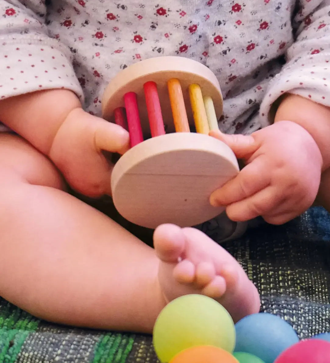 Baby holding a Grimms wooden mini rolling wheel
