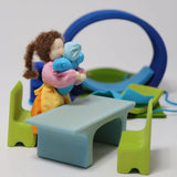 Grimm's blue and green mobile dolls home wooden toy play set table and chairs with Grimm's dolls placed besides it.