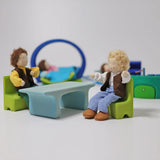Grimm's blue and green mobile dolls home wooden toy play set table and chairs with dolls seated on the chairs.
