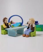 Grimm's blue and green mobile dolls home wooden toy play set table and chairs with dolls seated on the chairs.
