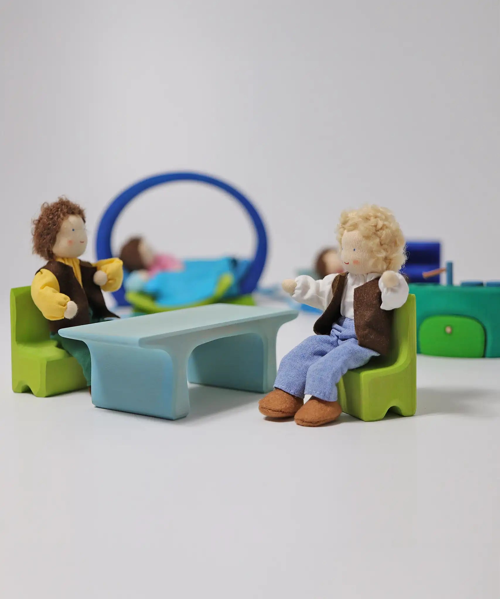 Grimm's blue and green mobile dolls home wooden toy play set table and chairs with dolls seated on the chairs.