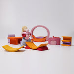 All the pieces from the Grimm's Pink Mobile Home wooden Toy Set laid out  in a small world play scene with a Grimms doll.