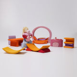 All the pieces from the Grimm's Pink Mobile Home wooden Toy Set laid out  in a small world play scene with a Grimms doll.