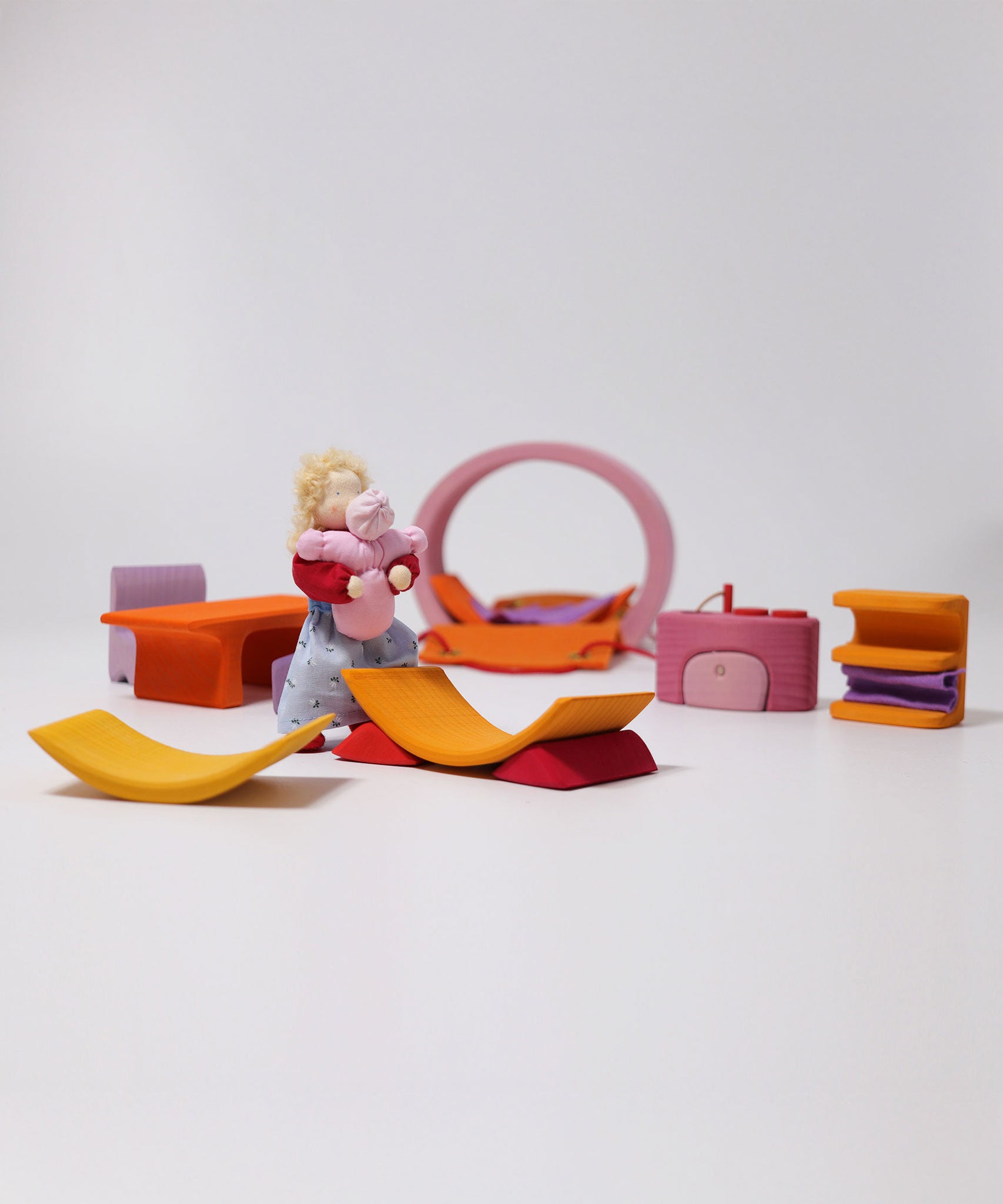 All the pieces from the Grimm's Pink Mobile Home wooden Toy Set laid out  in a small world play scene with a Grimms doll.