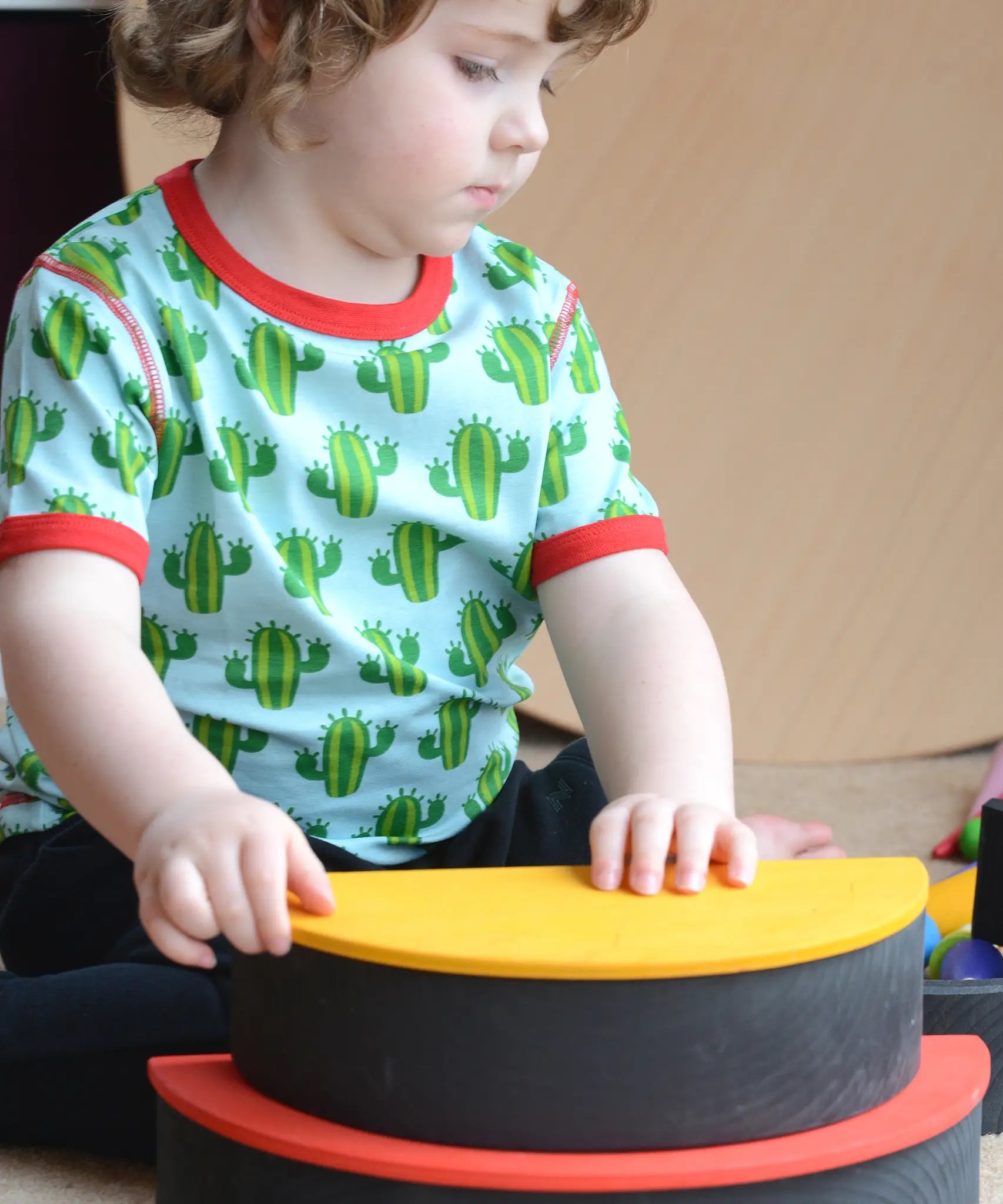 Child building a stack using Grimms monochrome arch and rainbow semi circle pieces