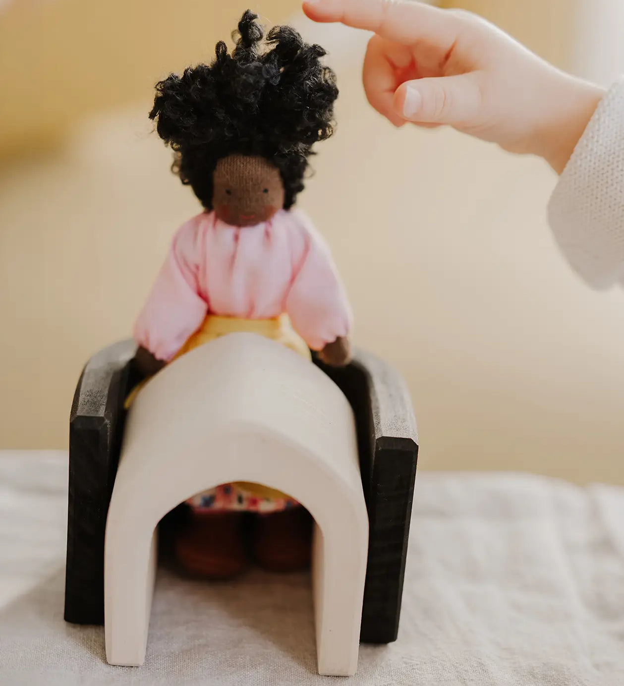 Small child pointing at a waldorf doll sitting on a Grimms wooden monochrome piece showing scale