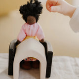 Small child pointing at a waldorf doll sitting on a Grimms wooden monochrome piece showing scale