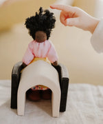 Small child pointing at a waldorf doll sitting on a Grimms wooden monochrome piece showing scale