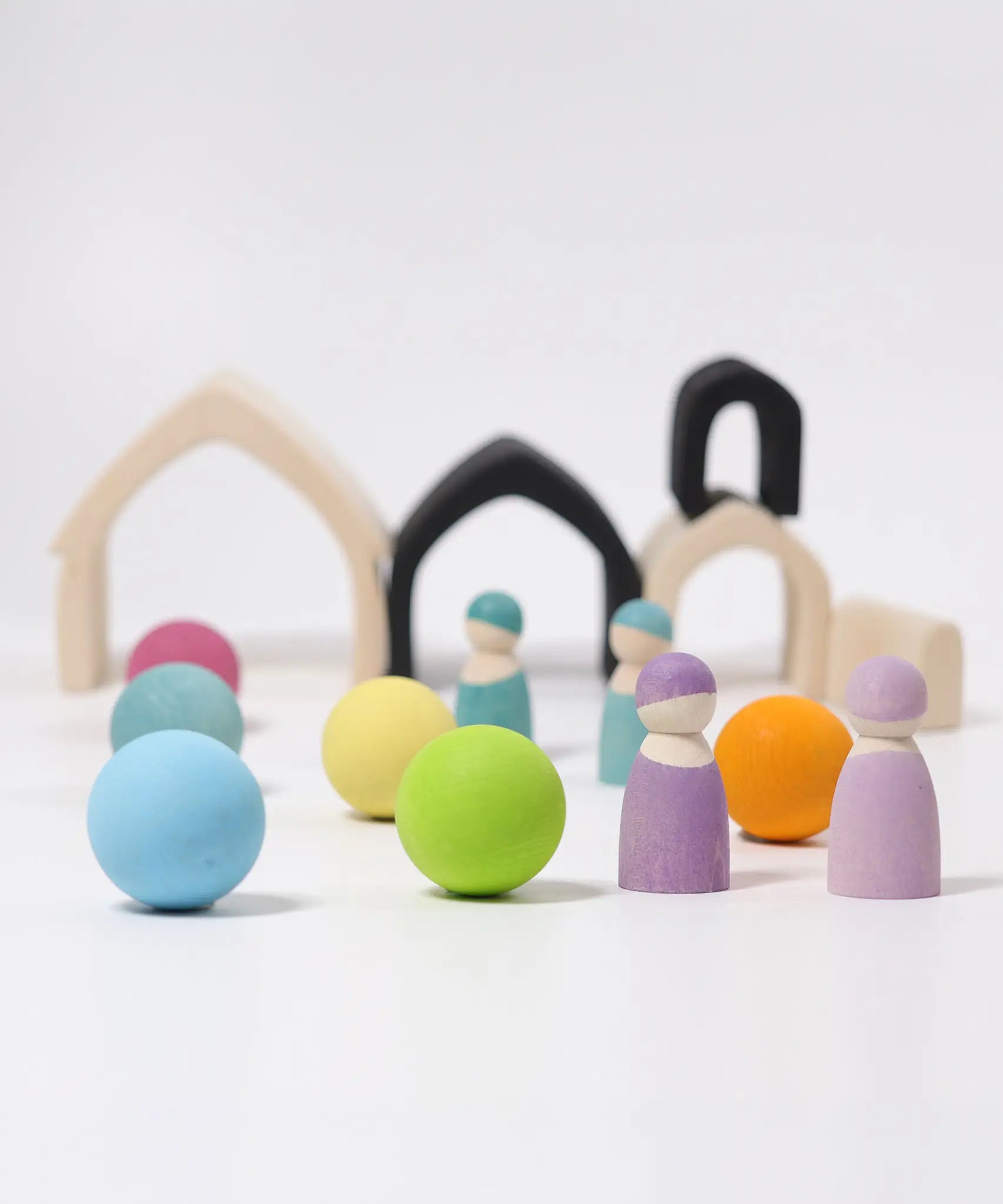 Loose Grimms wooden monochrome house pieces next to pastel balls and peg dolls in a play setup
