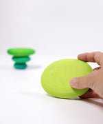 An adult's hand holding one of the pebbles from the Grimm's moss green pebble set in their hand.