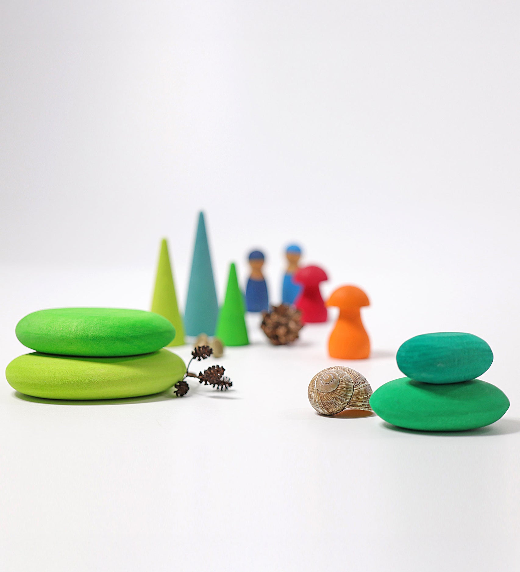 The Grimm's moss green wooden pebbles shown alongside a snail shell and nature finds with other Grimms wooden toys seen in the background.