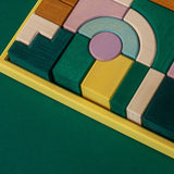 Grimm's wooden movement building set, shows handcrafted piece in a yellow frame on a green background.