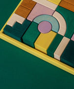 Grimm's wooden movement building set, shows handcrafted piece in a yellow frame on a green background.