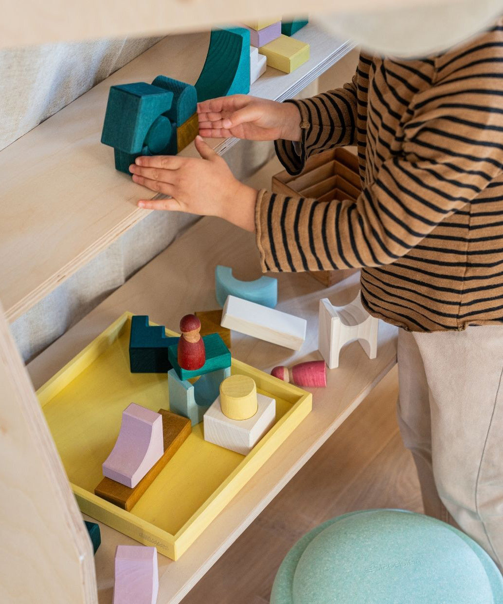 Child stacking using green hand carved wooden pieces from the Grimms movement set on a shelf