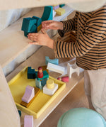 Child stacking using green hand carved wooden pieces from the Grimms movement set on a shelf