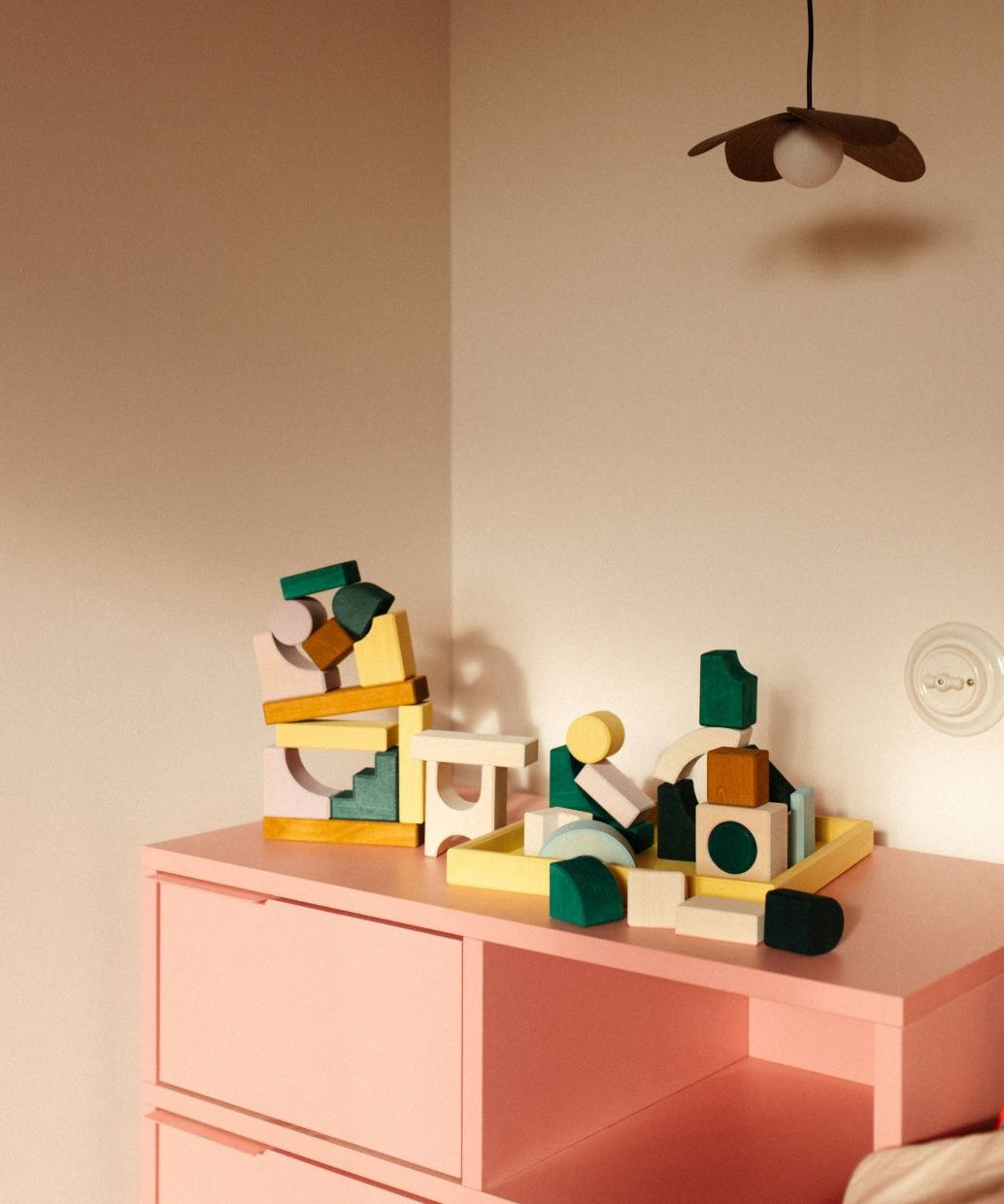 Loose pieces from the Grimms movement hand crafted building set on a pink drawer in a bedroom setting