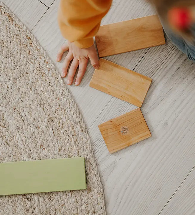 A chid hand next to loose Grimms wooden natural building boards showing scale
