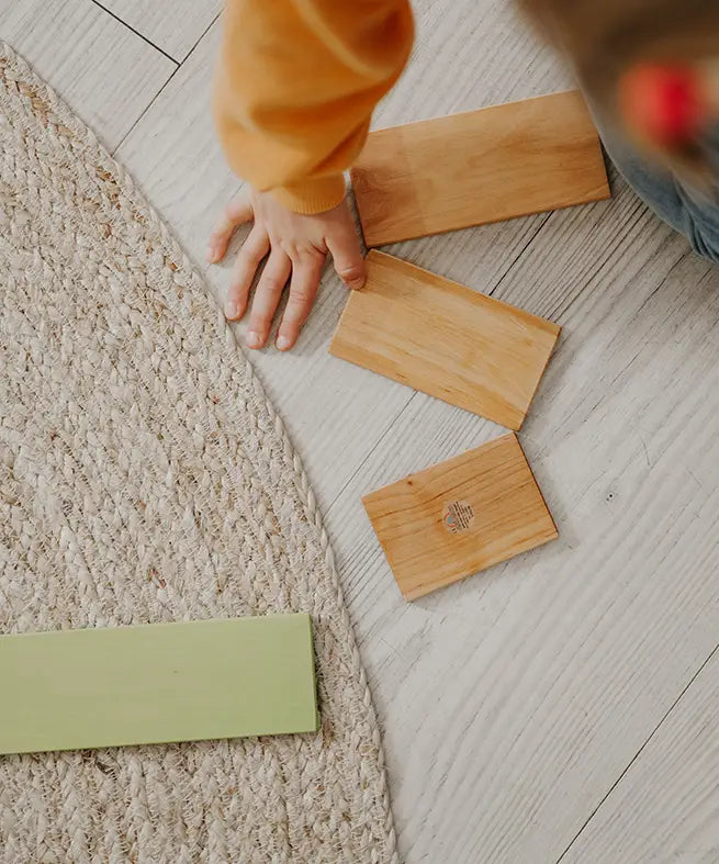 A chid hand next to loose Grimms wooden natural building boards showing scale