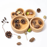 Overhead view of the Grimms natural wooden bowls with acorns and pinecones inside them