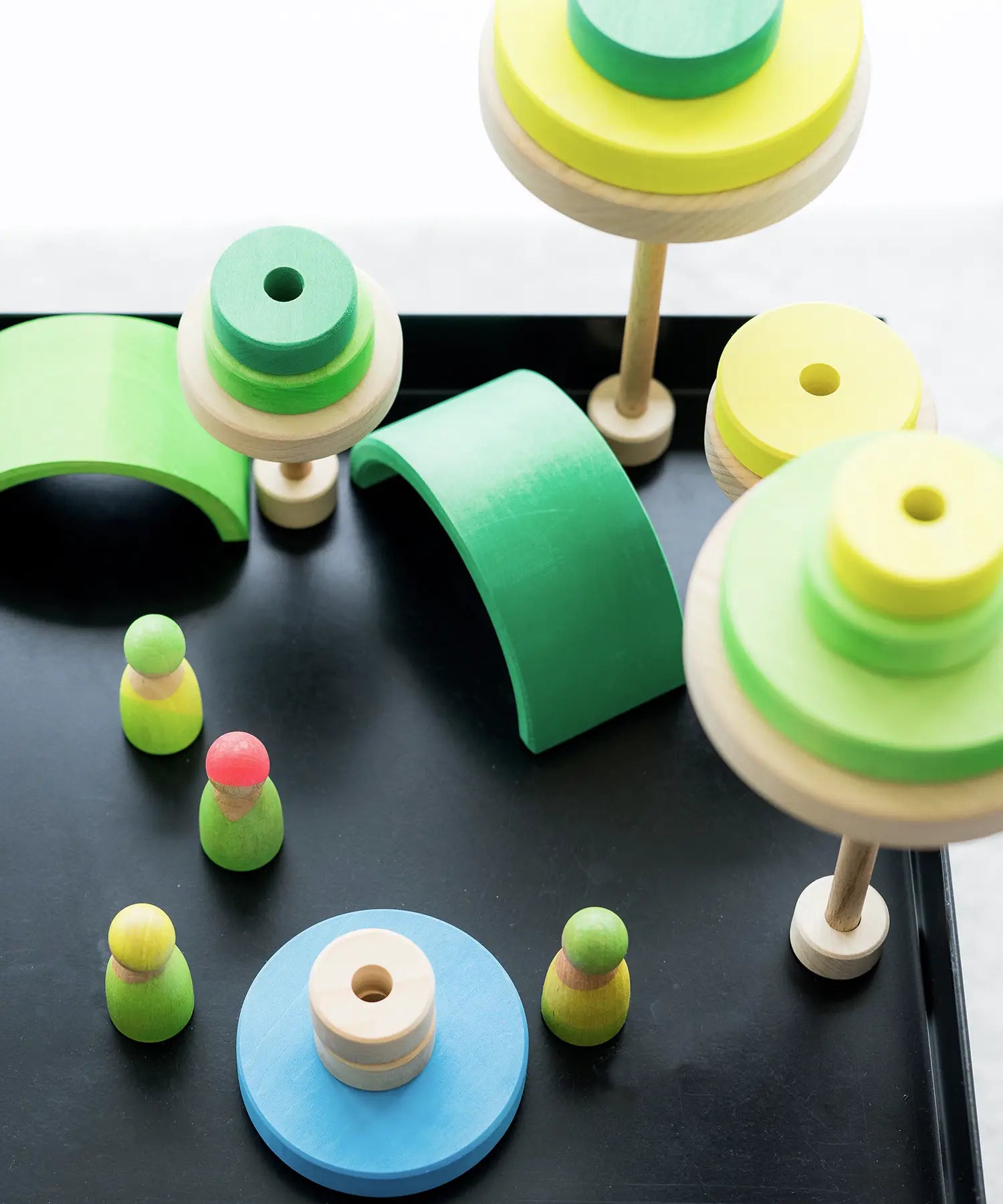 A small world made from neon green Grimms wooden conical pieces, arches and peg dolls