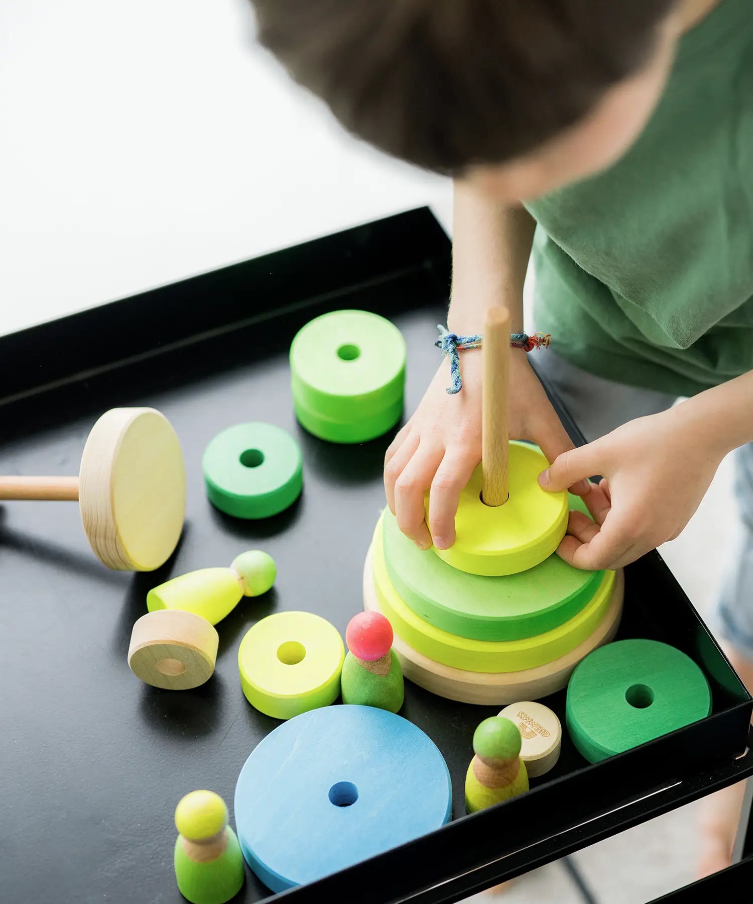 Child stacking the Grimms handcrafted wooden neon green conical pieces 