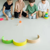 Children rolling loose Grimms wooden neon conical pieces on the floor. 