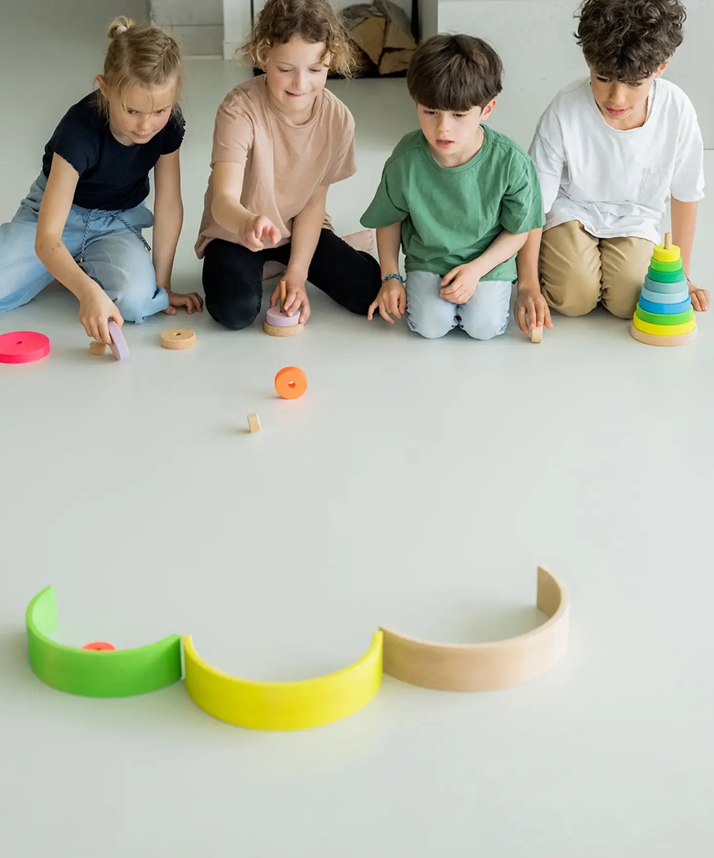Children rolling loose Grimms wooden neon conical pieces on the floor. 
