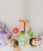 Children lying on the floor with the Grimms neon pink and green conical towers next to their heads