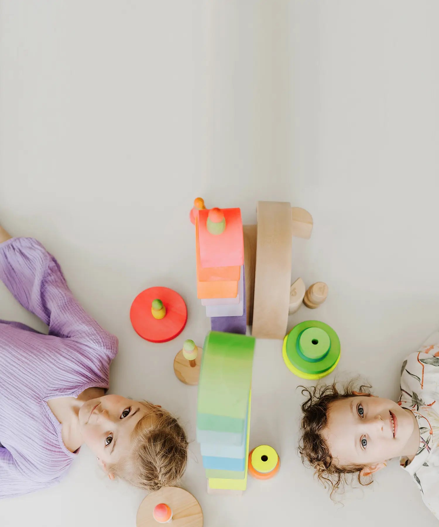 Children lying on the floor with the Grimms neon pink and green conical towers next to their heads