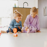 Children rolling different pieces from the Grimms wooden neon pink conical tower on the floor