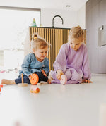 Children rolling different pieces from the Grimms wooden neon pink conical tower on the floor