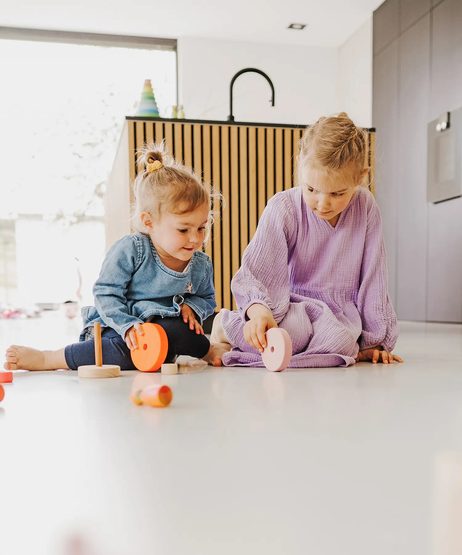 Children rolling different pieces from the Grimms wooden neon pink conical tower on the floor
