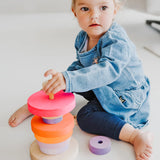 Child stacking different sized Grimms wooden conical pieces in neon pink