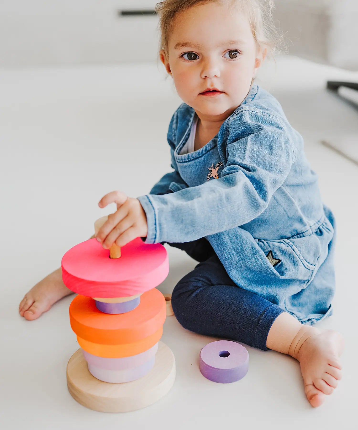 Child stacking different sized Grimms wooden conical pieces in neon pink