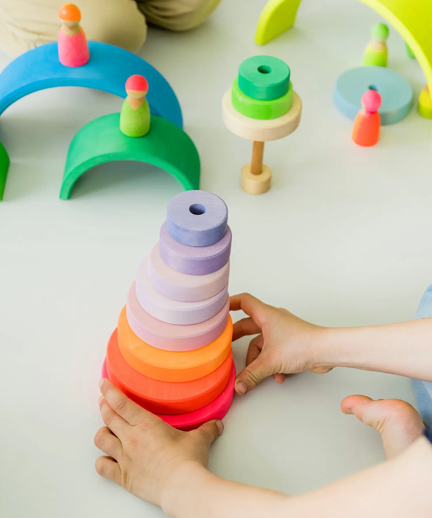 Child holding a stack made from loose Grimms neon pink wooden conical pieces