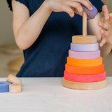 Child stacking pieces from the Grimms neon pink conical tower on the natural base 
