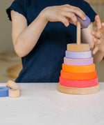 Child stacking pieces from the Grimms neon pink conical tower on the natural base 