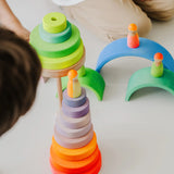 Stack of Grimms wooden neon pink conical pieces standing  next to loose neon green building blocks