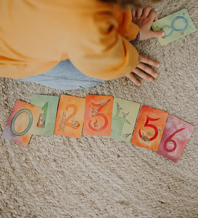 Child sorting the Grimms number cards from 0 to 6. Each card showing a corresponding number of illustrated animals
